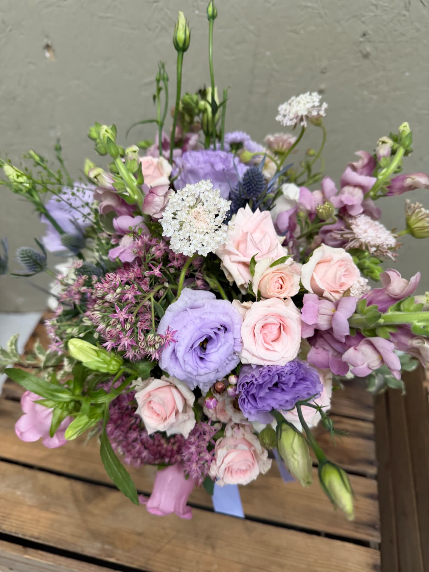 Arrangement of blush roses, lilac lisianthus and purple snapdragons on a wooden table