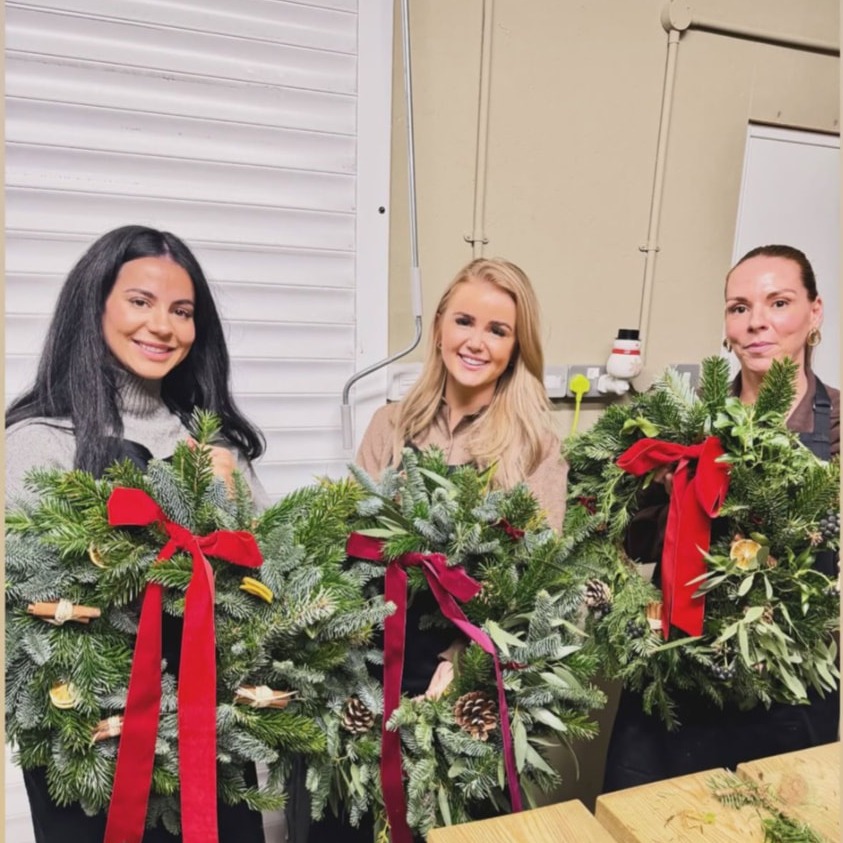 Three guests holding finished wreaths with dried oranges and red velvet ribbon