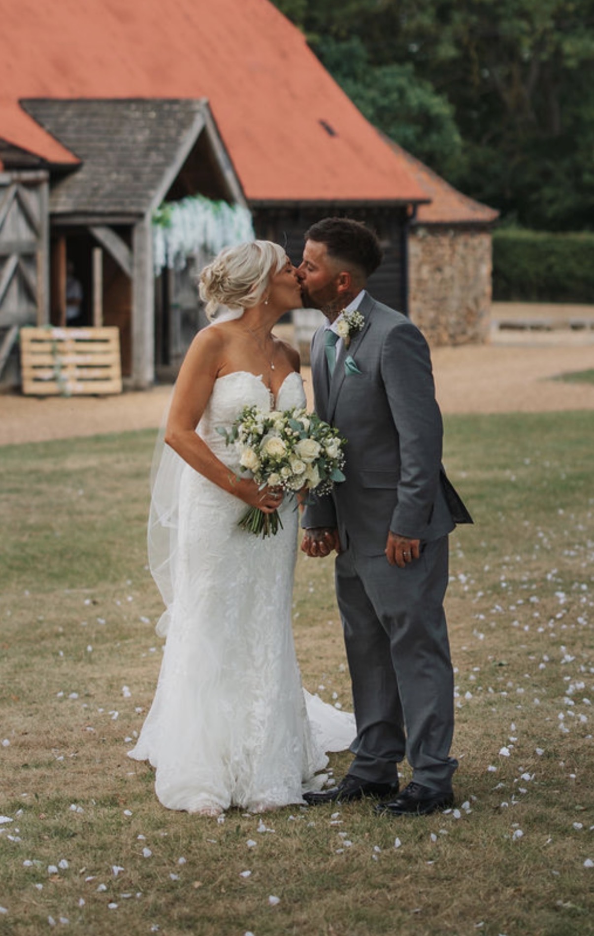 Bride and groom kissing beside a barn, the bride holding her bouquet