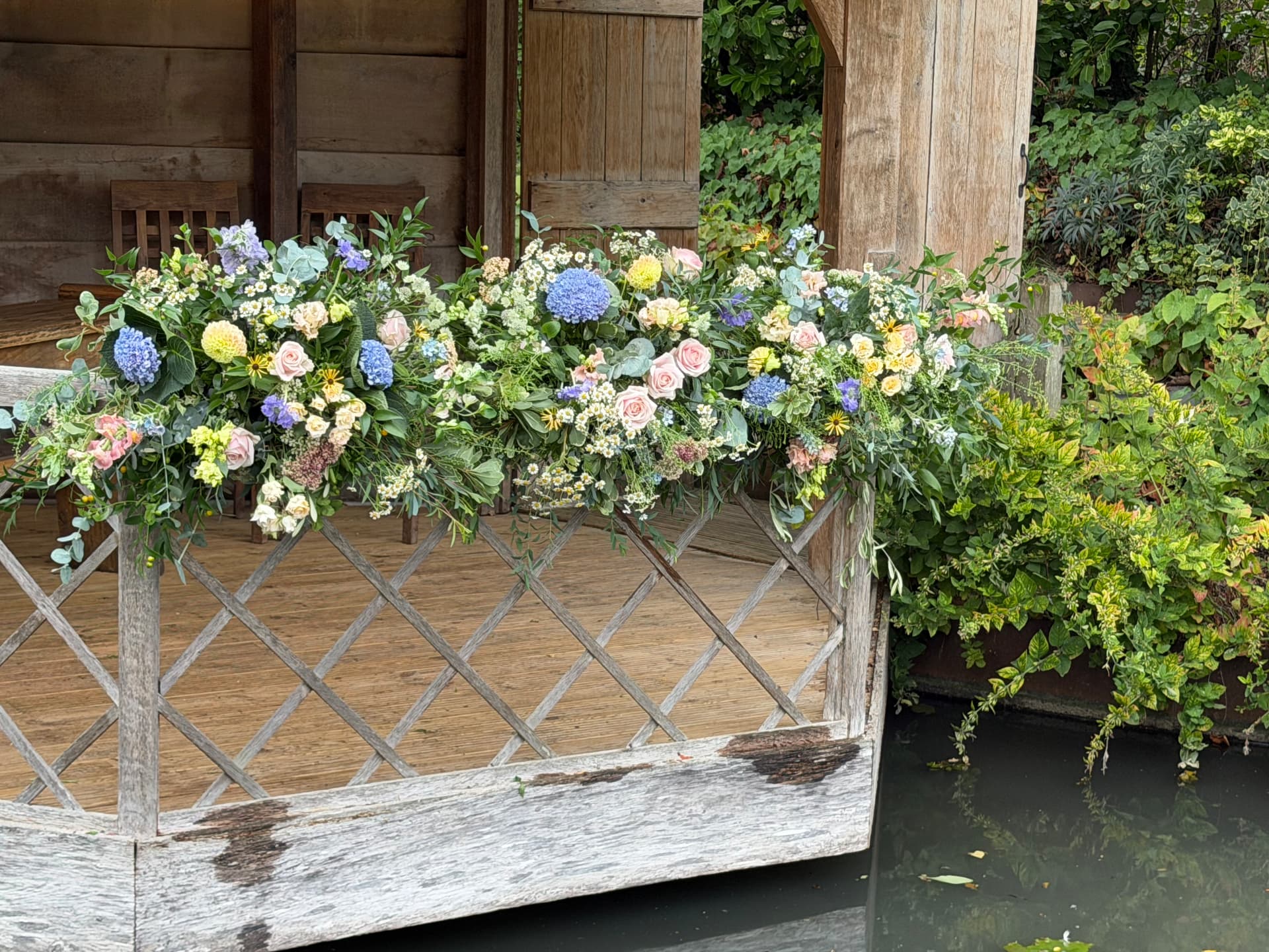 Blue hydrangeas, blush roses and yellow dahlias arranged along a wooden gazebo balustrade