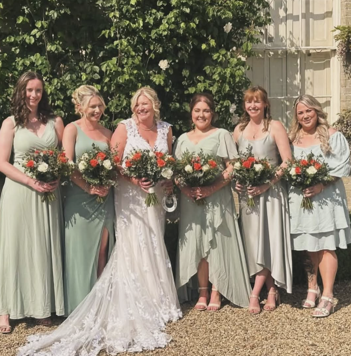 Bride with bridesmaids in sage dresses holding coral and ivory rose bouquets