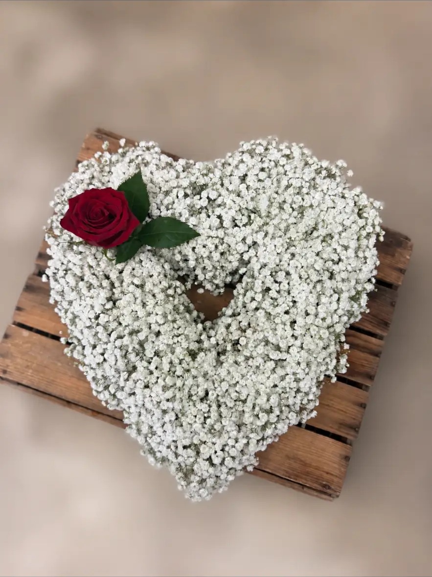 Overhead view of a heart-shaped gypsophila tribute wreath with a red rose