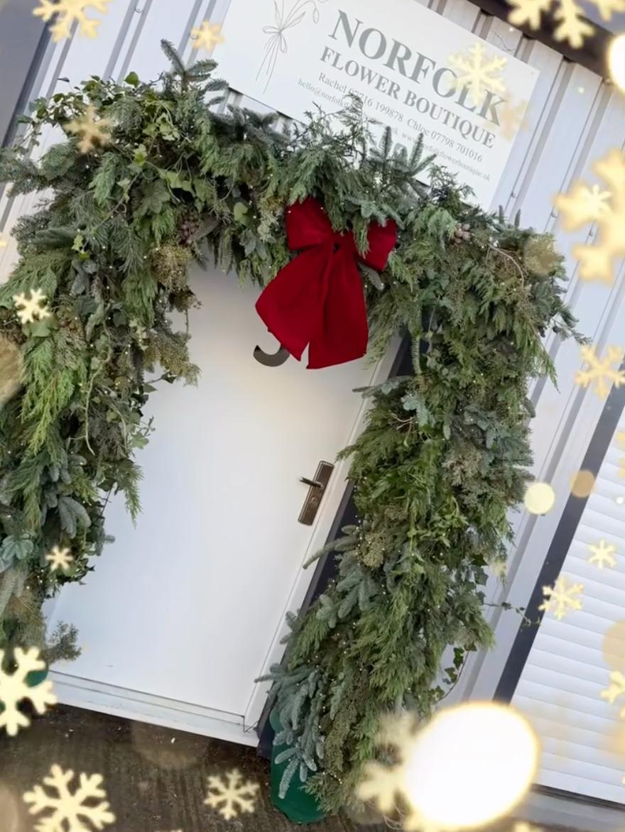 The Norfolk Flower Boutique studio door dressed with a fresh evergreen garland and red velvet bow