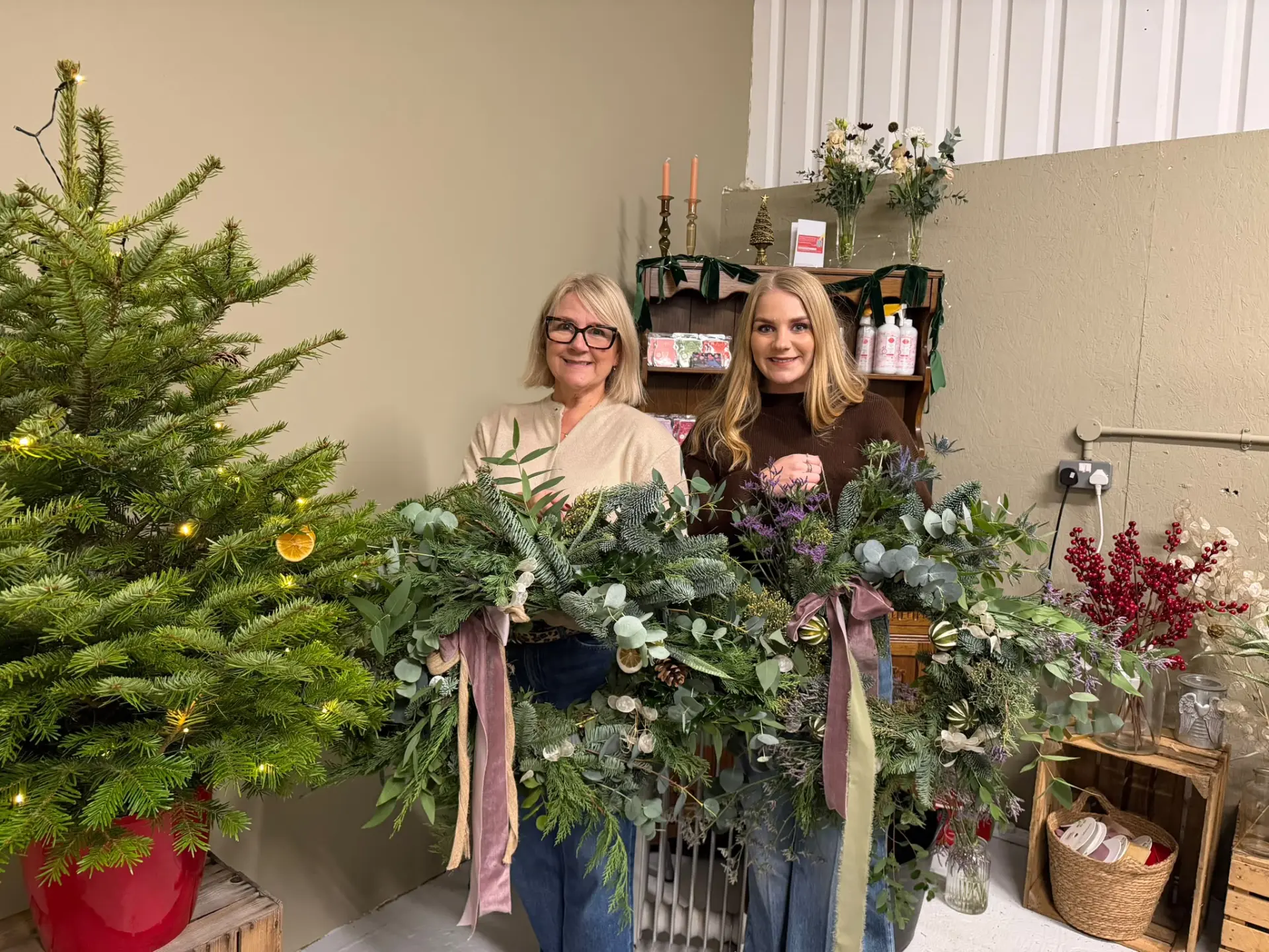 Two guests proudly holding their finished wreaths with dried oranges and velvet ribbon