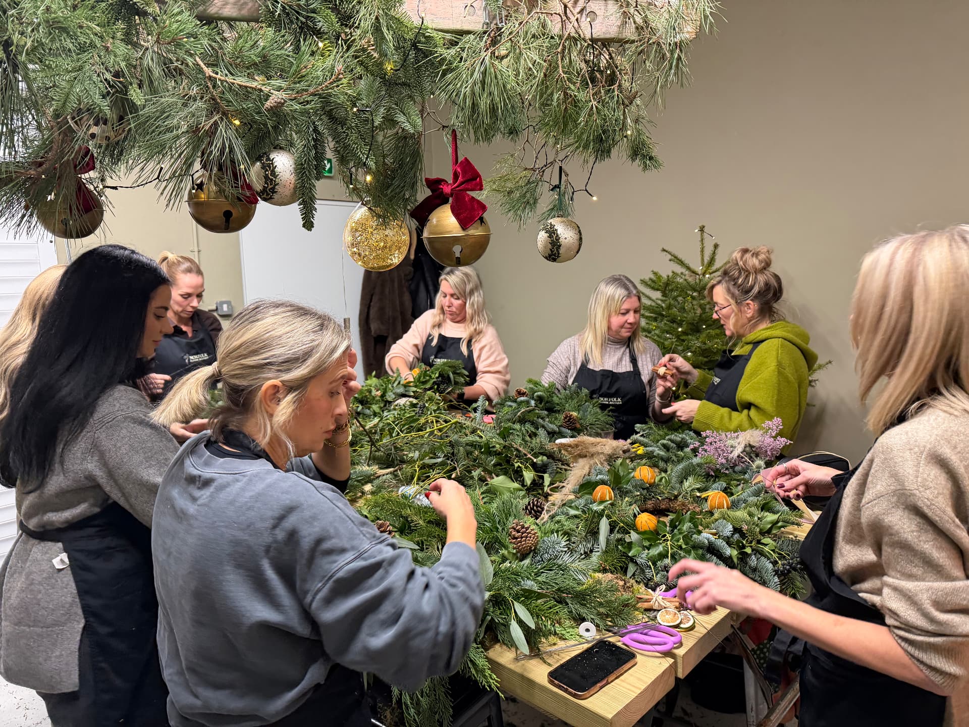 Guests making wreaths at a workshop table beneath a hanging pine canopy