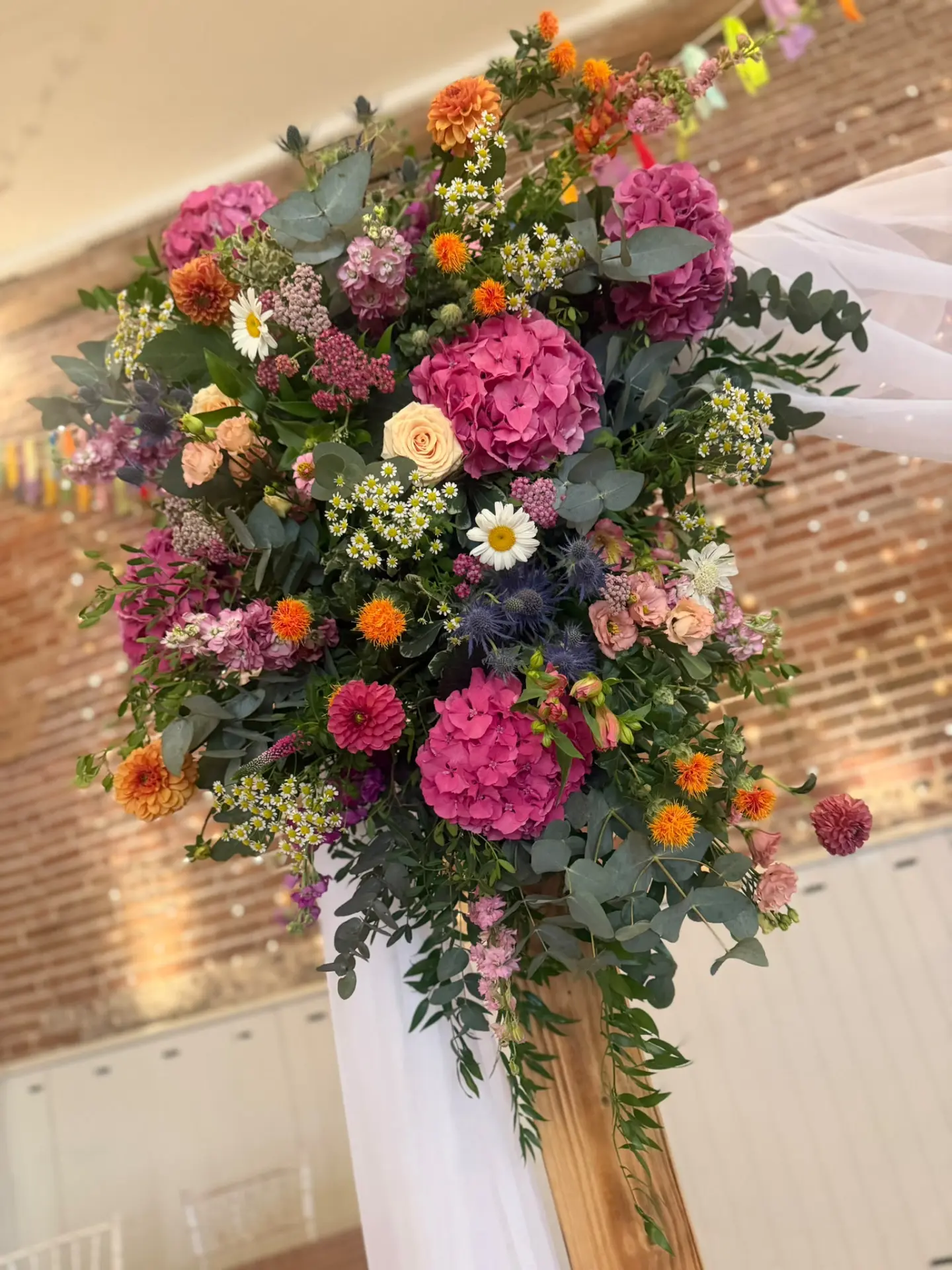 Colourful ceremony arch detail with pink hydrangeas, orange dahlias and blue sea holly