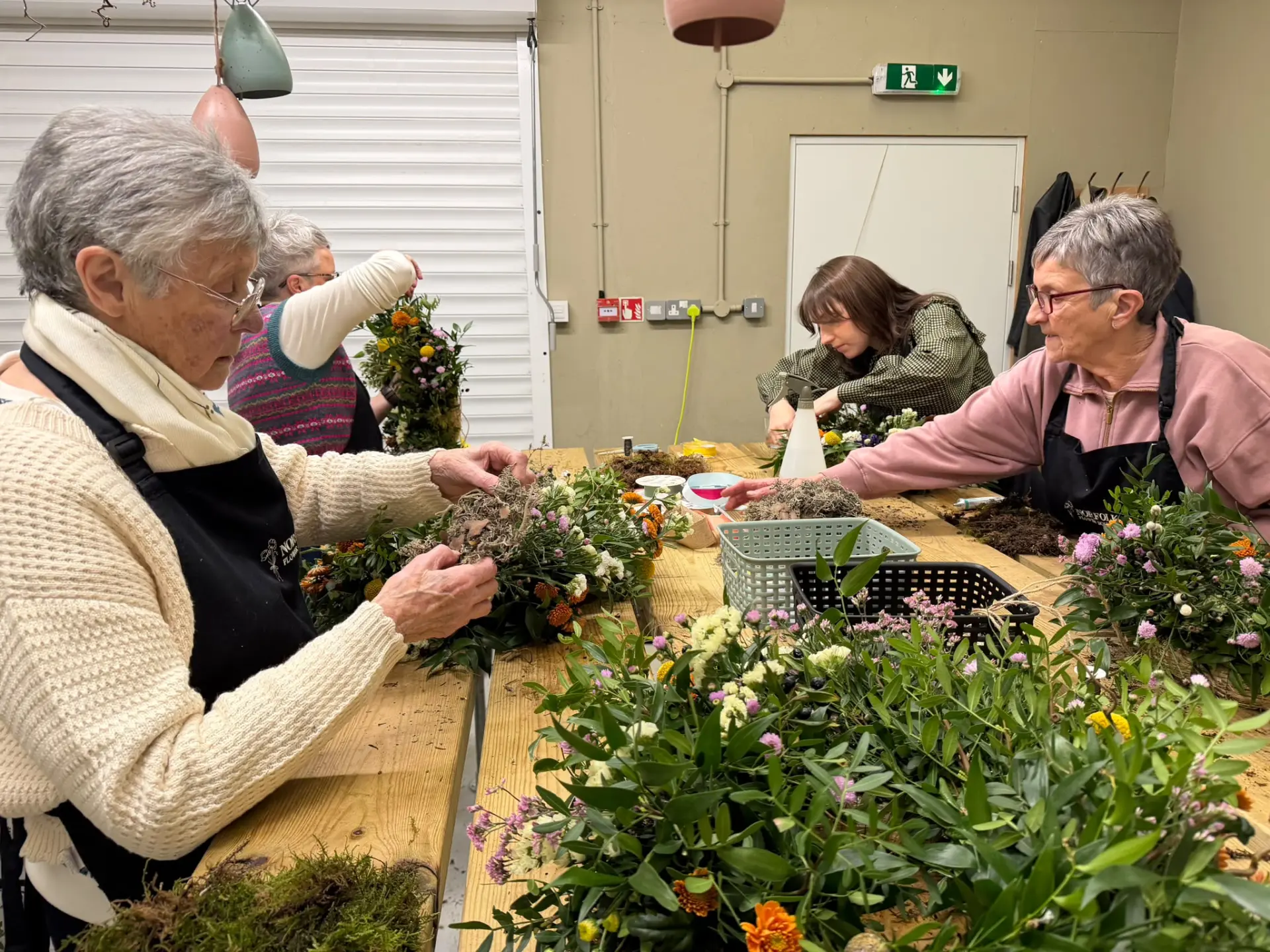 Four guests working on seasonal floral arrangements around long wooden tables