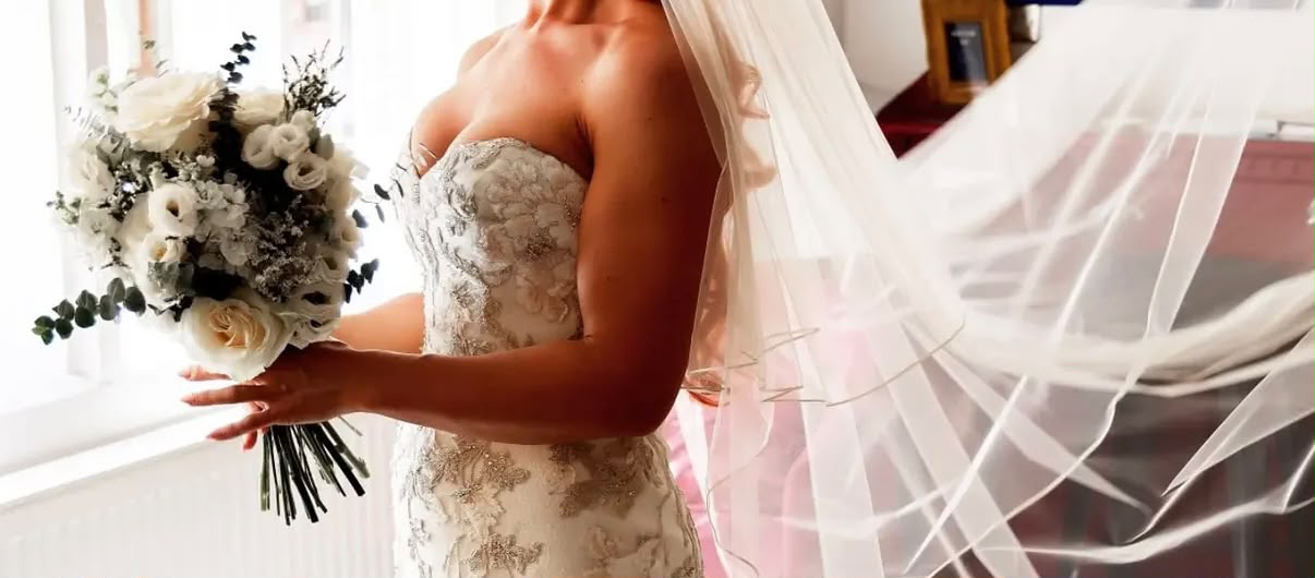Bride in profile holding a cream rose and eucalyptus bouquet with her veil lifting in the breeze