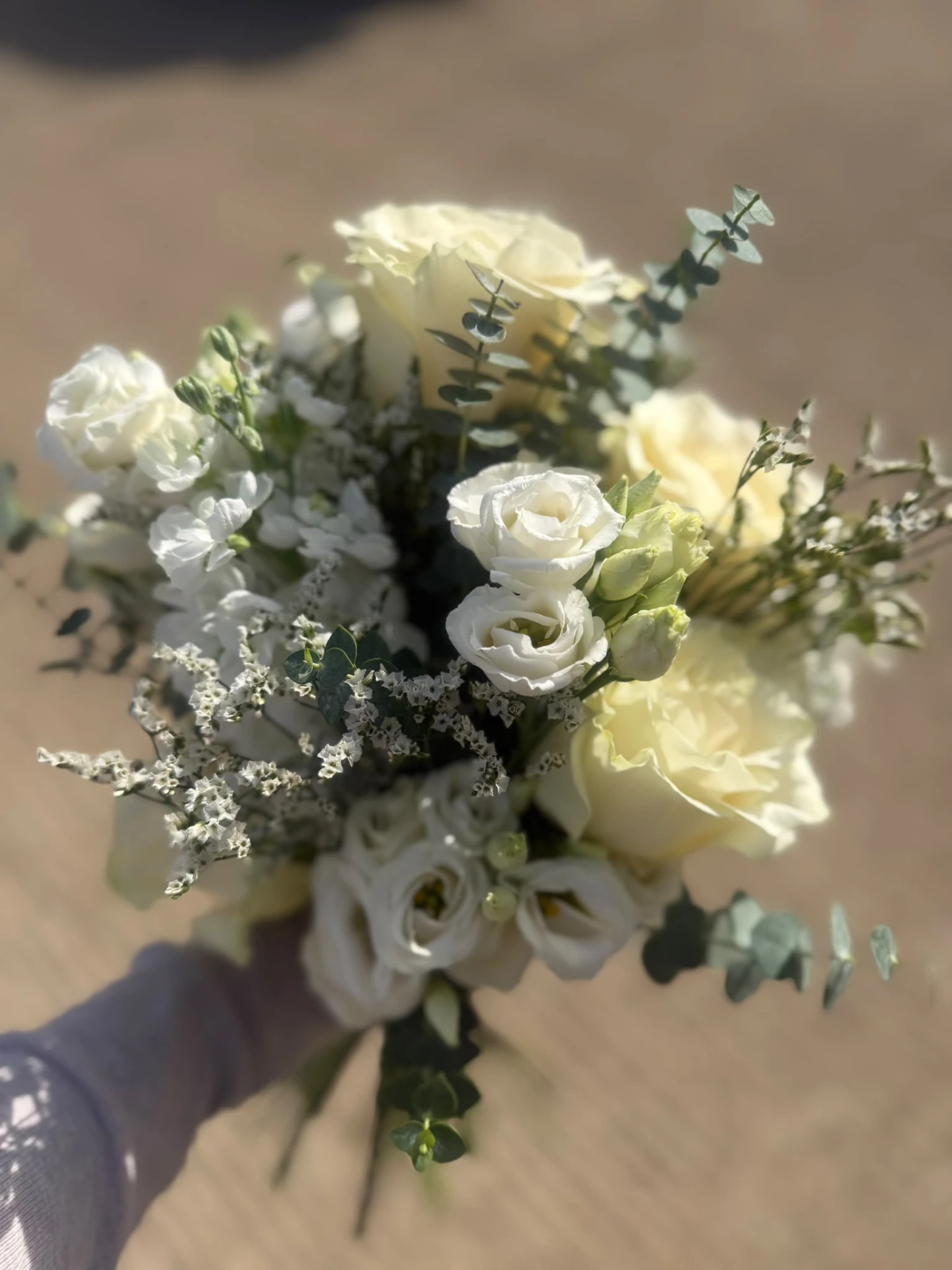 Top-down close-up of a bridal bouquet of cream roses, lisianthus and silver eucalyptus