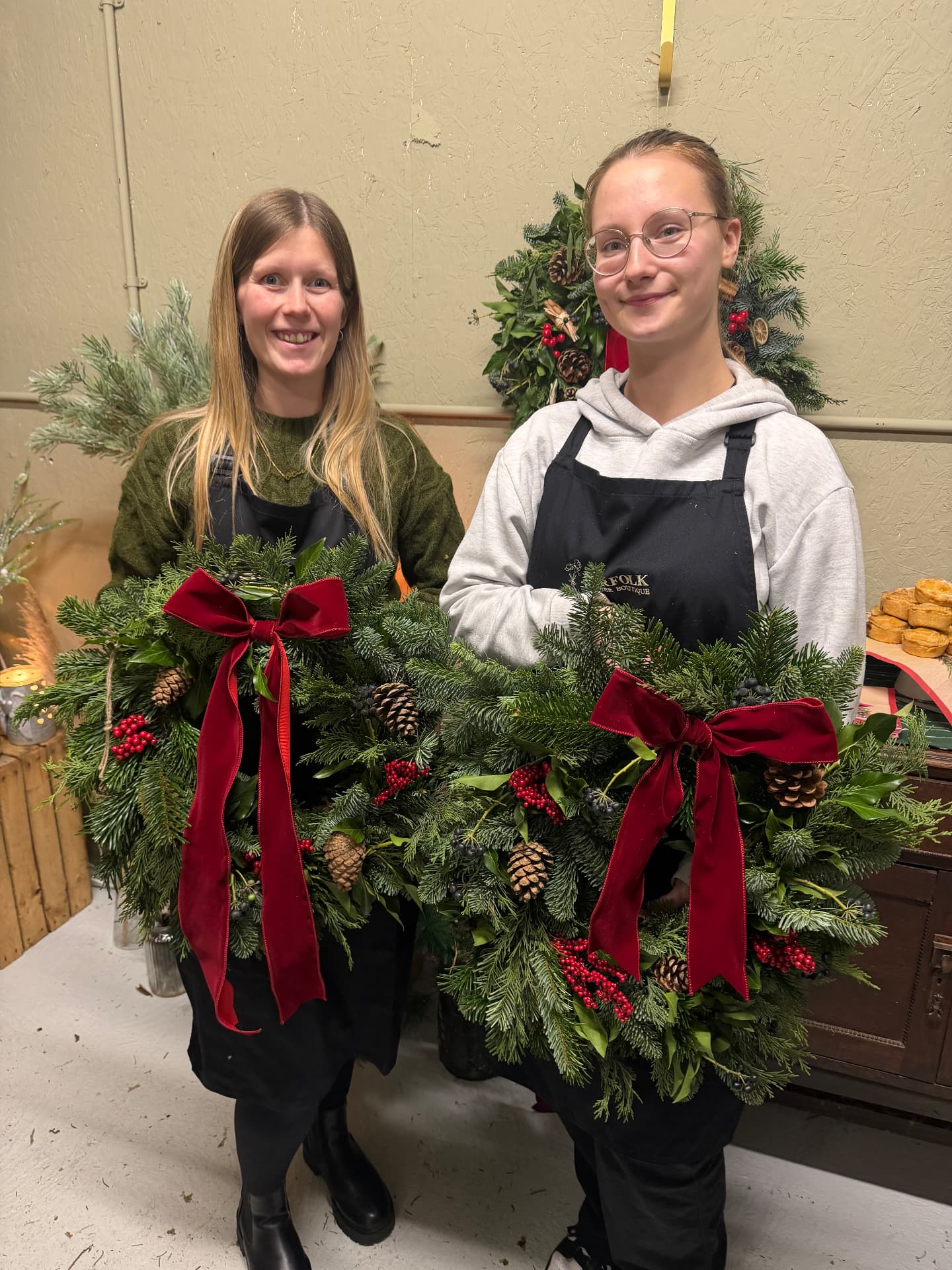 Two women in aprons holding their finished Christmas wreaths
