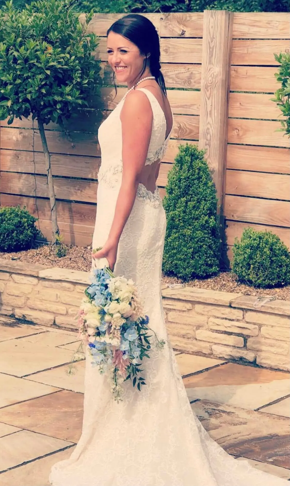 Bride in a lace gown with a cascading blue, cream and pink bouquet