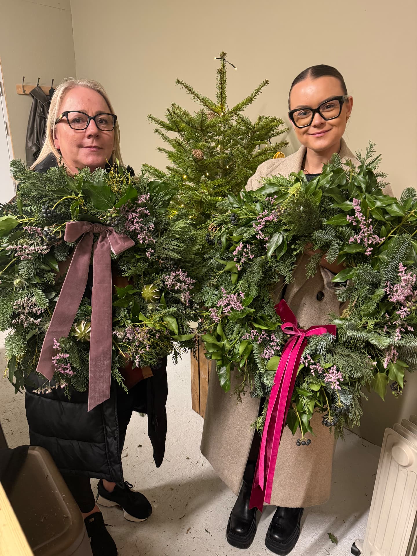 Two guests holding their finished Christmas wreaths with velvet ribbon