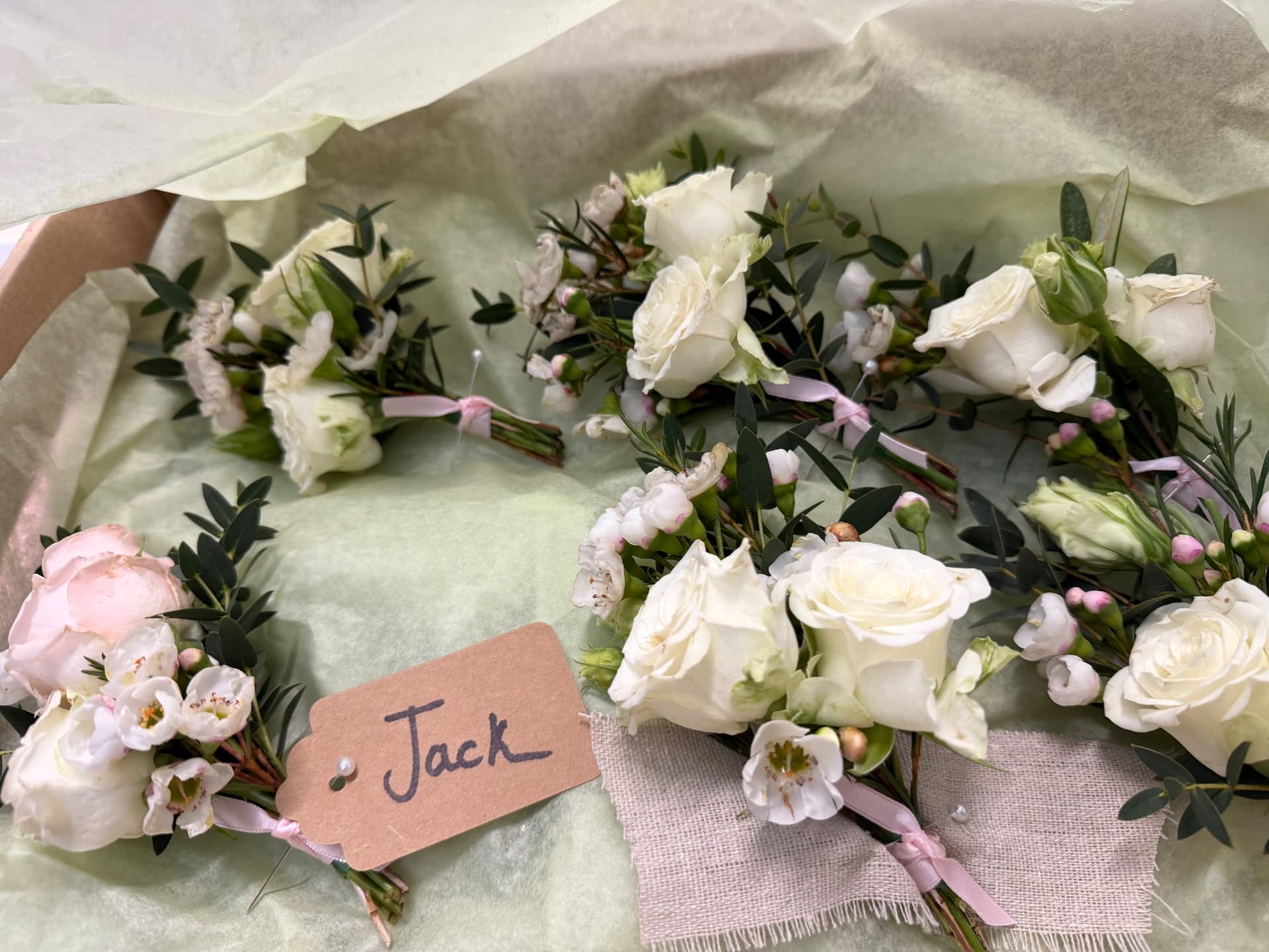 White rose buttonholes with eucalyptus laid in a lined box with a handwritten name tag