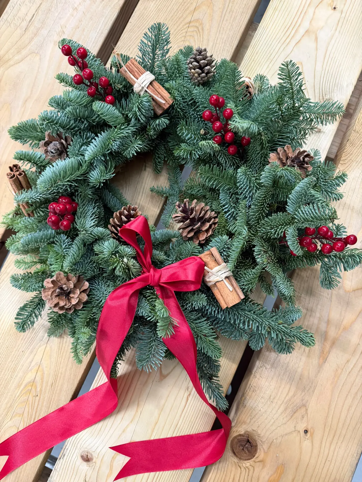 Fresh evergreen Christmas wreath with red berries, pine cones, cinnamon sticks and a red satin bow