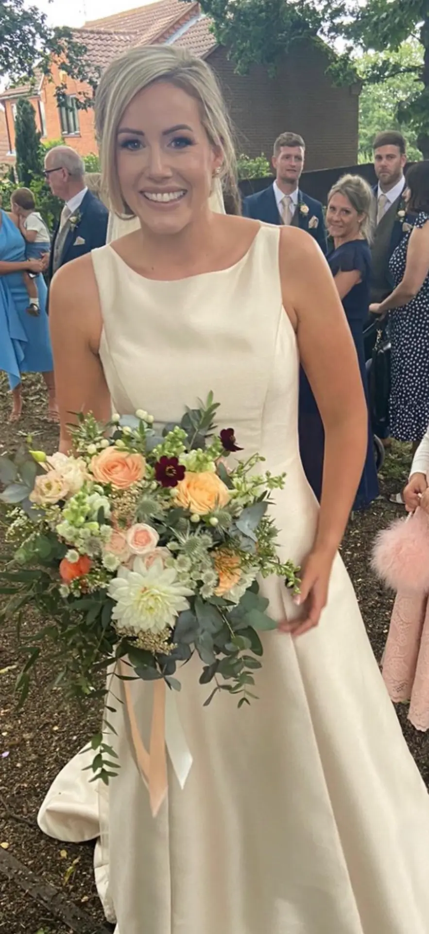 Smiling bride in an ivory dress holding a peach, cream and burgundy bouquet