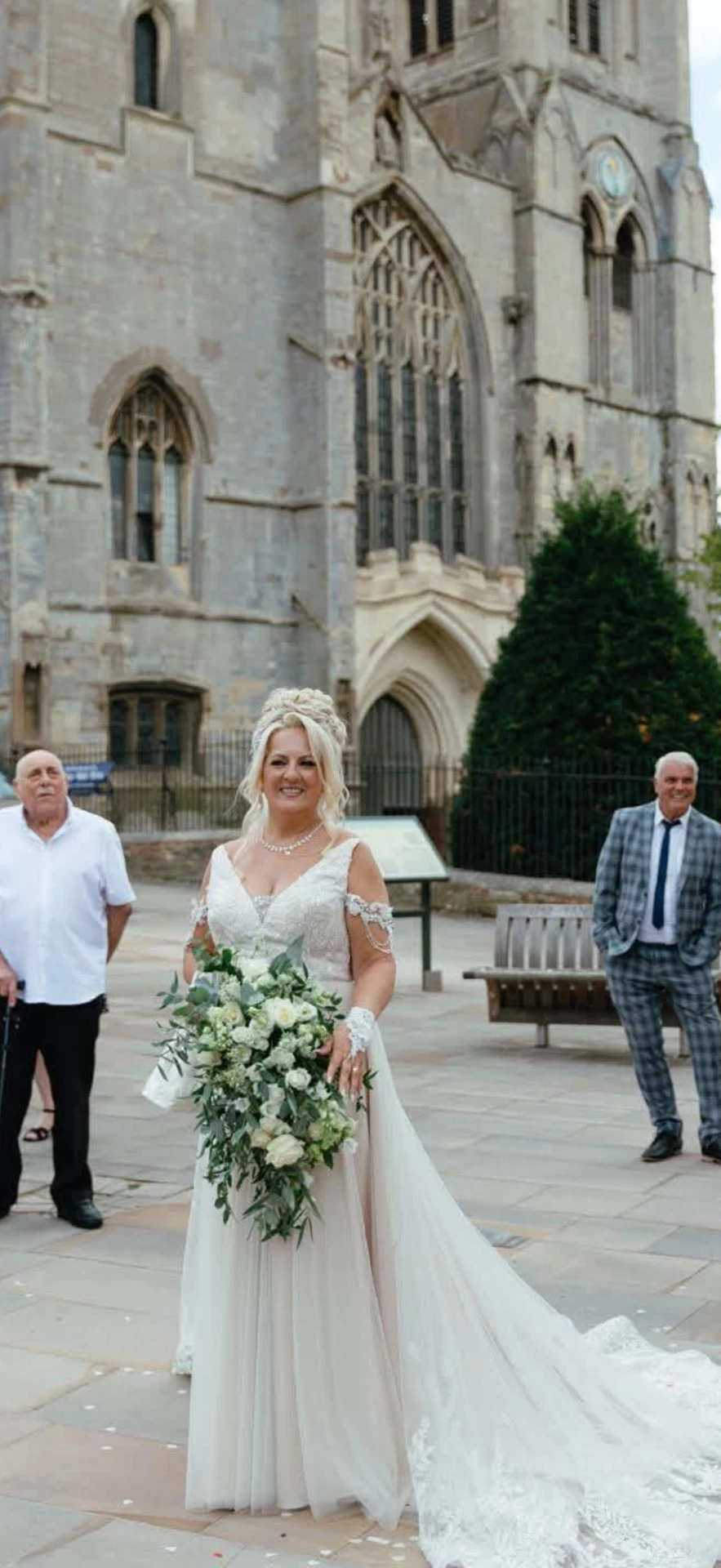 Bride in a white gown holding a cascading white bouquet in a stone church plaza
