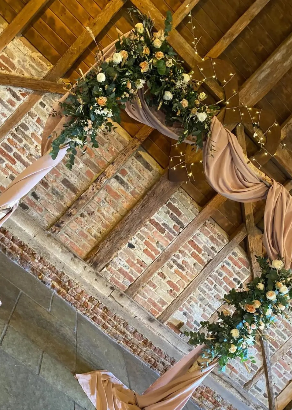 Draped barn archway dressed with ivory and peach roses, eucalyptus and fairy lights